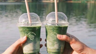 two matcha cups being held in two different hands doing a cheers in front of a lake background