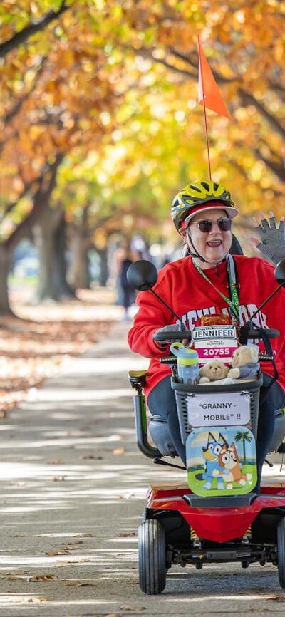 Woman in red on a mobility scooter riding on a autumnal tree lined path.