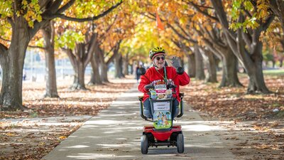 Woman in red on a mobility scooter riding on a autumnal tree lined path.