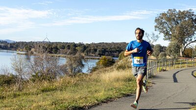 Runner runs alongside lake on bike path with parliament house in the background