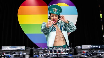 DJ Sexy Galexy at SpringOUT Fair Day Dj Sexy Galexy boi drag performer and DJ playing music at Fair day Large Rainbow Heart in the backgr