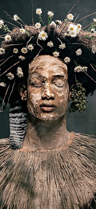 Photograph of a serene young man with eyes closed, with clay body paint, a collar of wild grasses.
