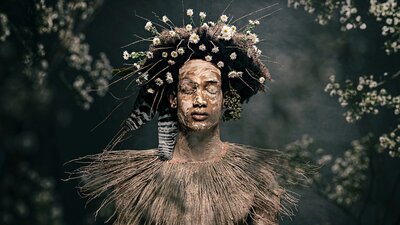 Photograph of a serene young man with eyes closed, with clay body paint, a collar of wild grasses.