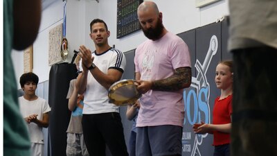 A group of adults and kids stand together playing music and clapping