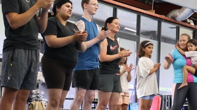 A group of adults and kids stand clapping and singing