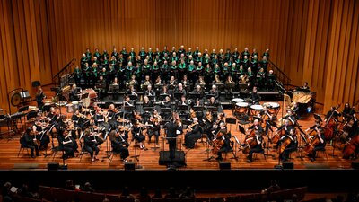 The Armed Man concert 5 July 2025 Large orchestra, piano and choir on stage with Louis Sharpe conducting.