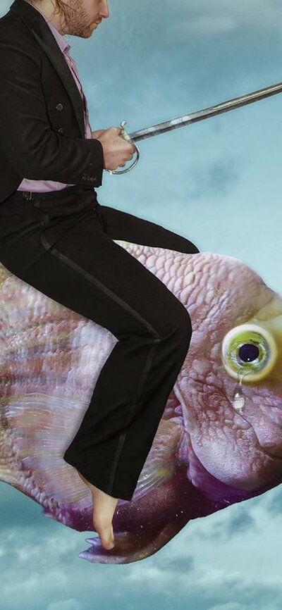 A man wearing a black suit riding a fish through the cloudy sky
