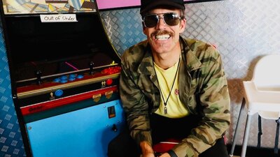 Man sitting down, smiling at camera, in front of game machine