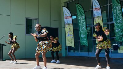 Dancers perform on an outdoor stage with banners saying 'Celebrate Gungahlin' and 'Gungahlin Arts'.