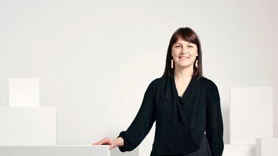 Phoebe Porter standing by white plinths and gallery wall smiling