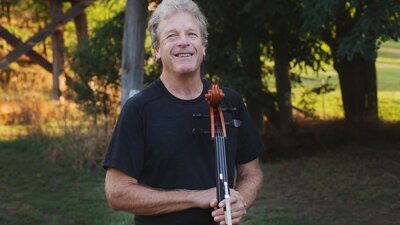 Man holding cello with trees and grass in the background