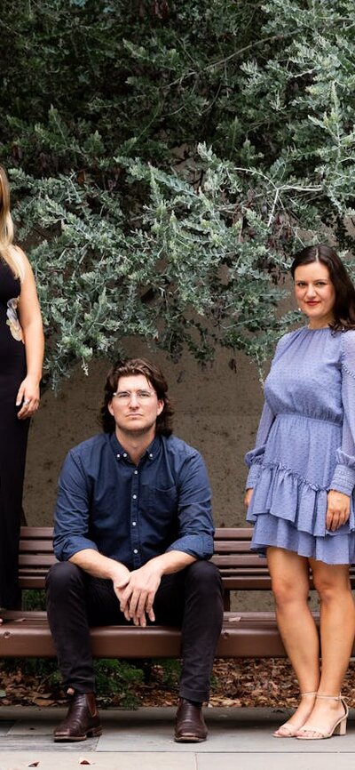 Five adults sitting on or standing around a bench outside.
