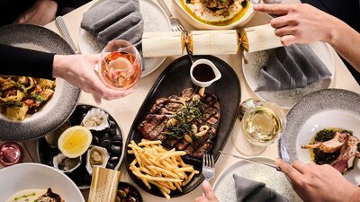 A photo of a dinner table of food with peoples hands holding bon bons and wine for Christmas
