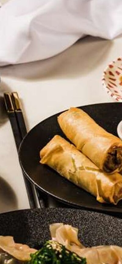 Platters of spring rolls, money bags and gyozas on a white table.