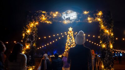Christmas in July Christmas tree Woman standing in front of the festival's entry with Christmas lights and tree