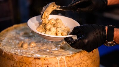 Cheesy gnocchi Someone serving gnocchi with cheese from a big cheese wheel