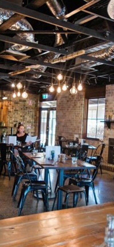 Image of 1882 Hall's interior with wooden tables, black chairs and brick walls