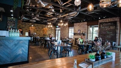 Image of 1882 Hall's interior with wooden tables, black chairs and brick walls