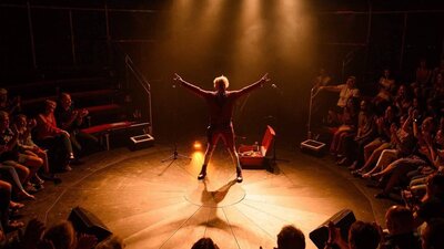 The Wham Glam Circus Man delivers rock'n'roll laughs and gasps with his superfun family street show A lone performer poses ready for a comedy circus show, surrounded by a crowd on three sides.