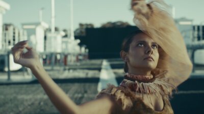An image of a woman dancing with arms in the air, outdoors and looking toward the sky