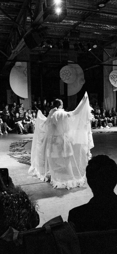 The audience sits in a large circle. In the middle, a figure in white holds a graceful pose.