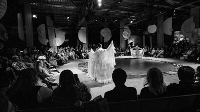 The audience sits in a large circle. In the middle, a figure in white holds a graceful pose.