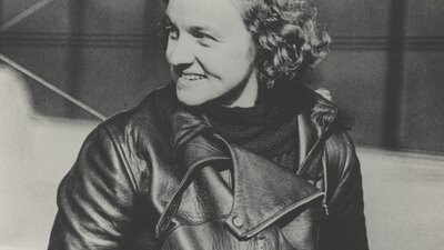 A sepia photograph of a woman with curly hair in flight gear.
