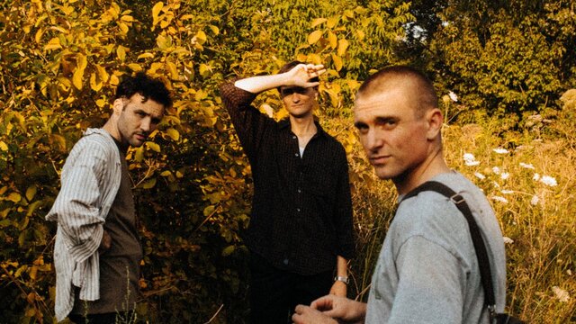 Three band members from Cola looking at the camera in a forest
