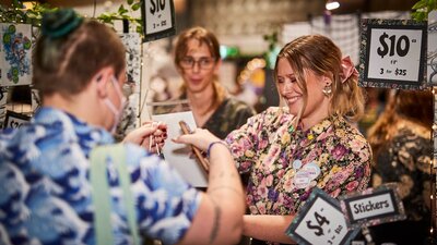 person in a blue shirt buying items from an artists table