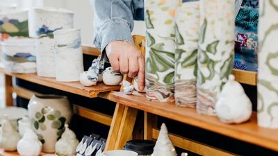 A hand touching some ceramic vessels on a market stall display
