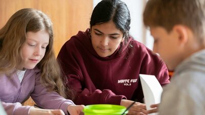 Three students are focused on an art project at a table.