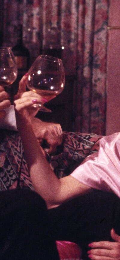 Woman wearing a pink gown with a wine glass clinking against another man's wine glass