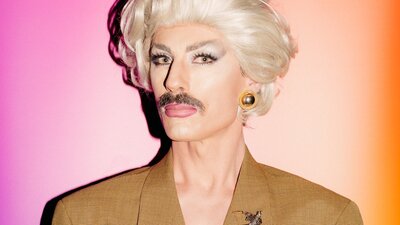 Drag artist man wearing a blonde wig and brown moustache