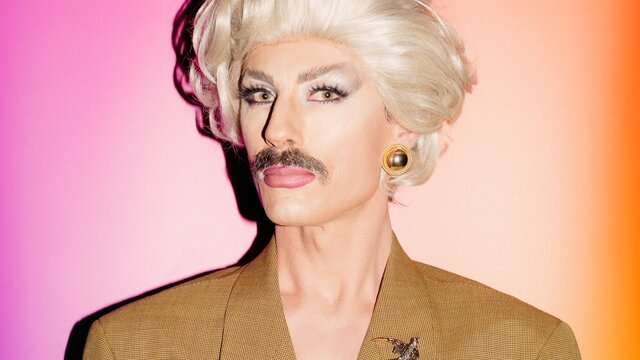 Venus Mantrap Drag artist man wearing a blonde wig and brown moustache