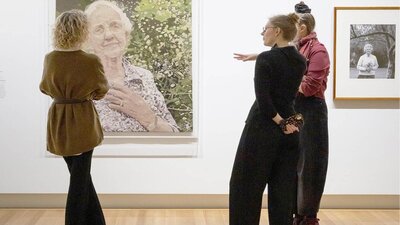 Three people view a weaved portrait of Dame Elisabeth Murdoch in a lush garden.