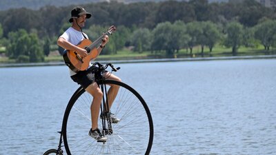 Simon playing a guitar while riding his penny-farthing