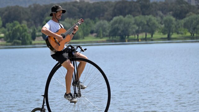A penny-farthing Simon playing a guitar while riding his penny-farthing