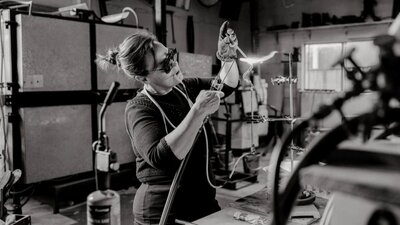 A black and white photograph of the artist with a blow torch  creating glass art