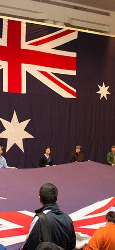 Children and adults hold a large Australian flag inside Parliament House.
