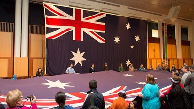 Children and adults hold a large Australian flag inside Parliament House.