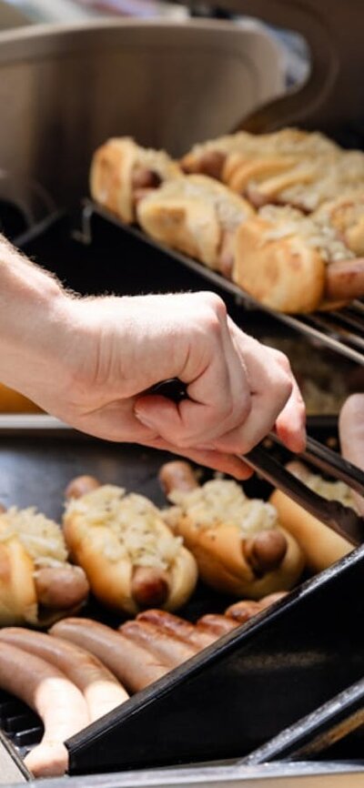 Close up of sausages cooking on a BBQ as a person uses tongs to turn them.