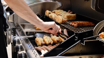 Close up of sausages cooking on a BBQ as a person uses tongs to turn them.