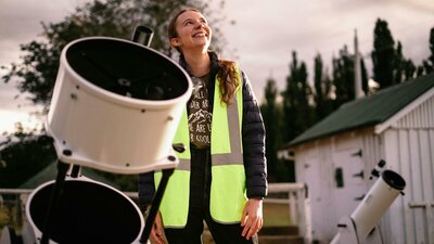 Young woman standing next to telescope looking towards the sky at Lanyon Homestead