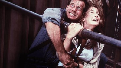 Man and woman hold onto metal pole struggling to not fly away