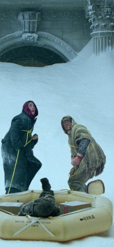 Two men in snow pulling a blow up boat looking scared and cold
