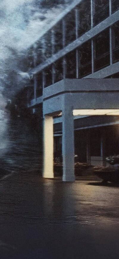 Still of two people running into a building while a wave larger than the image is coming towards the