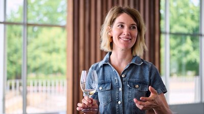 A woman holds a glass of wine and is gesturing with her other hand