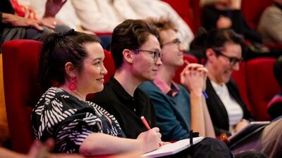 People sitting in a theatre smiling and listening to the speakers