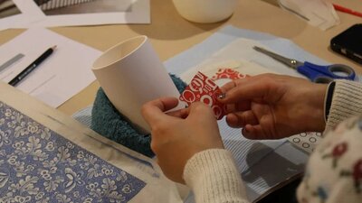 Ceramic Decal Decoration Workshop with Sarit Cohen, 2025 A close up shot of a pair of hands applying a red decal to a white ceramic cup