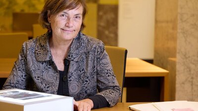A woman with brown hair is seated at a table, looking directly at the camera.